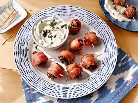 Bacon-wrapped figs on a blue and white plate with dipping sauce | Daily’s® Premium Meats