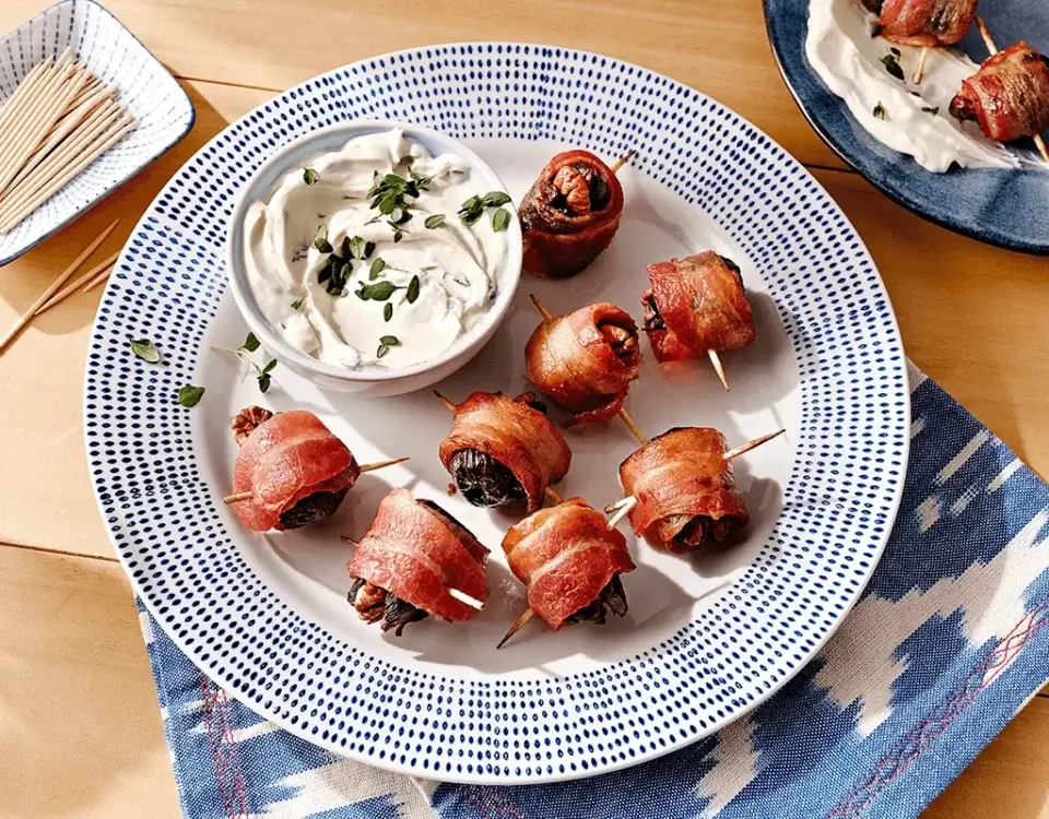 Bacon-wrapped figs on a blue and white plate with dipping sauce | Daily’s® Premium Meats